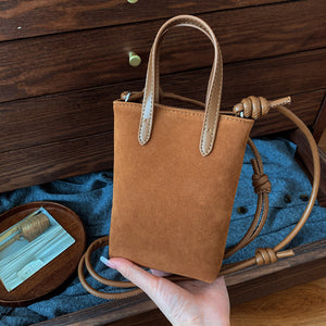 Brown leather handbag held by a hand on a wooden surface with blue fabric
