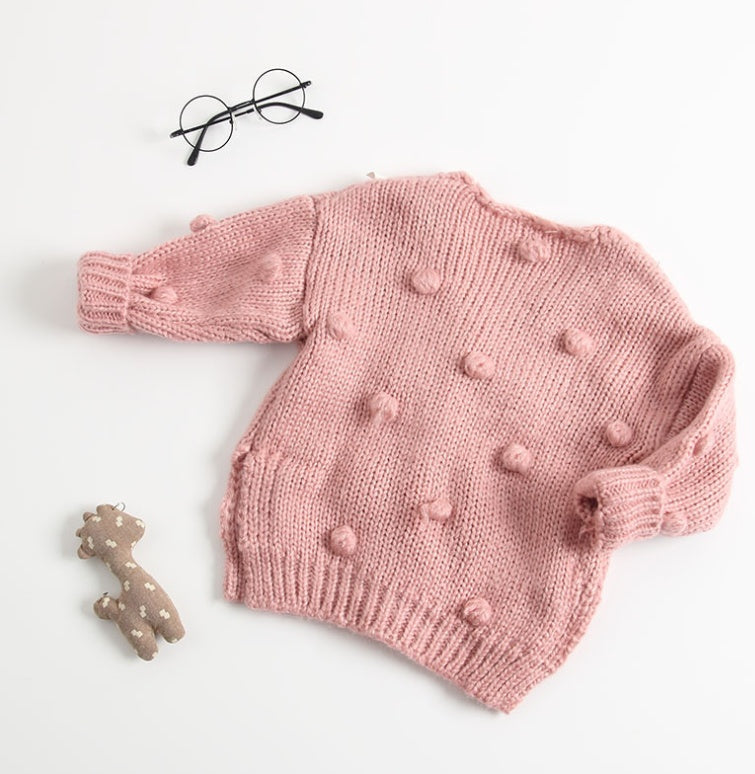 Pink knitted sweater with pom-poms on a light background