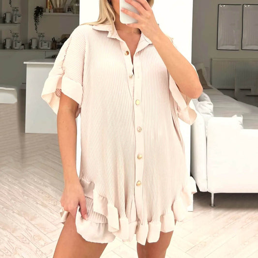 Woman wearing a light pink button-up dress in a room with white furniture.