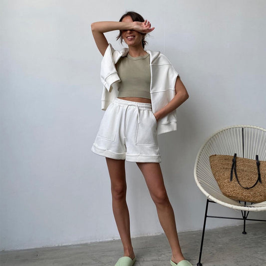 Woman in a casual outfit with shorts and a top, standing in a room with a chair and bag.