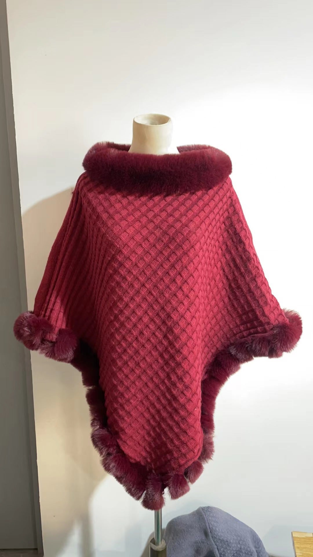 Red poncho with fur trim on a mannequin against a white wall.