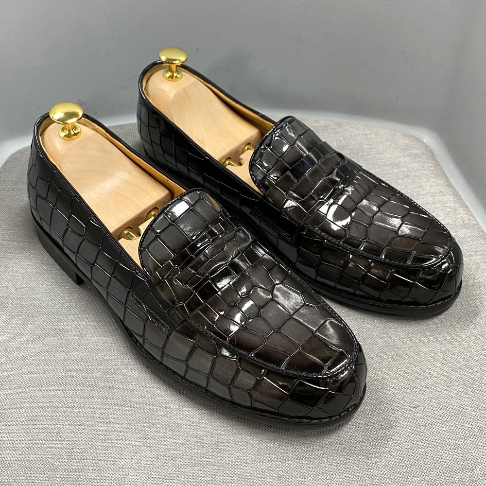 Black crocodile-patterned loafers on a light gray surface with a neutral background
