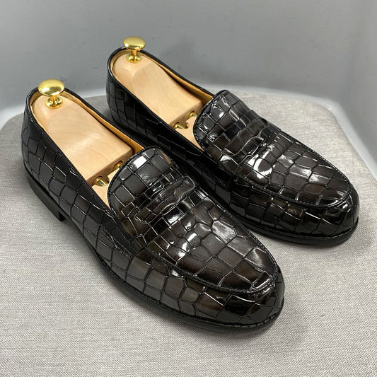 Black crocodile-patterned loafers on a light gray surface with a neutral background