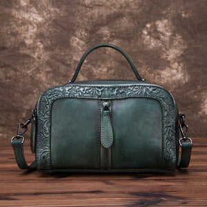 Green leather handbag with intricate patterns on a wooden surface and brown background