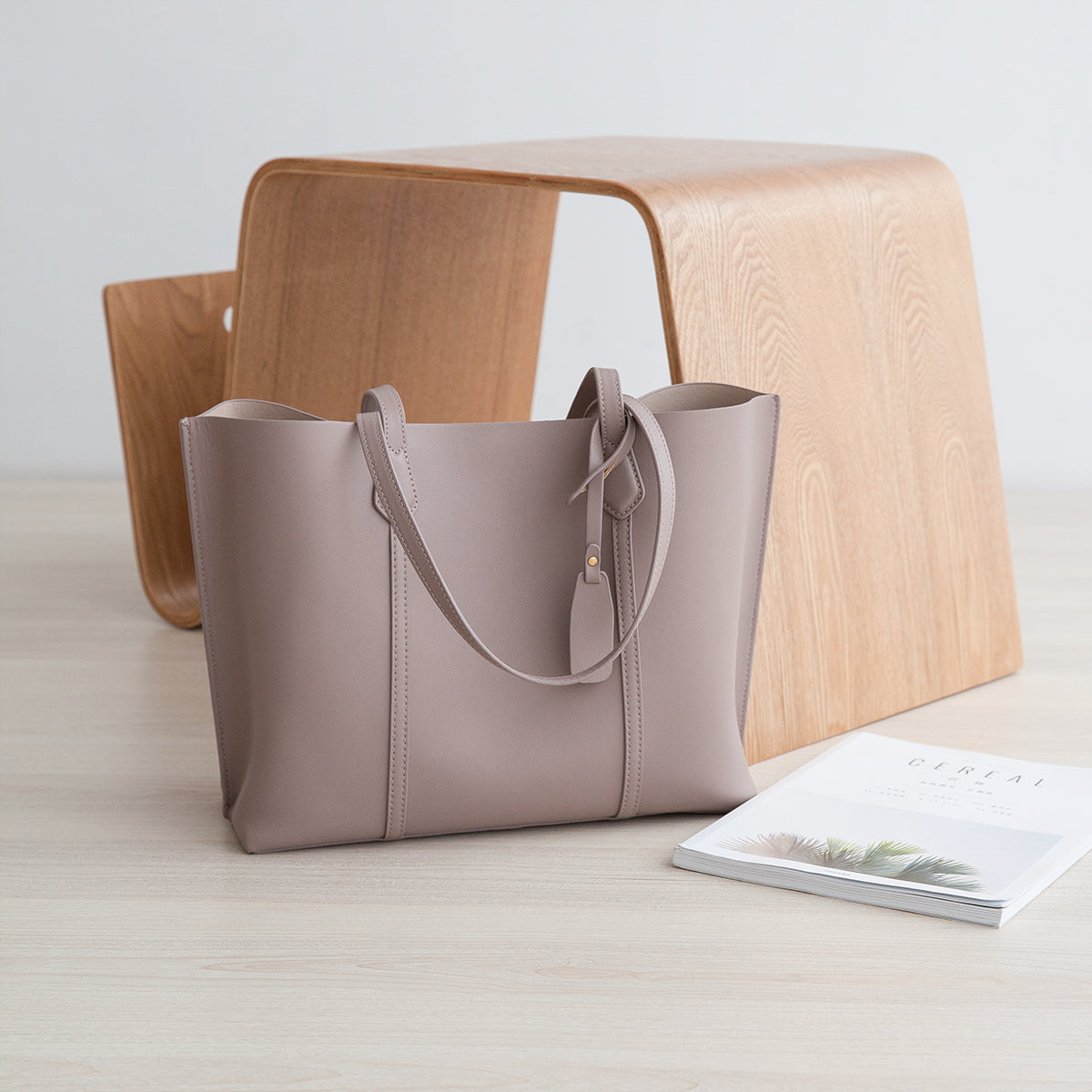 Beige handbag on a light wooden surface with a magazine underneath