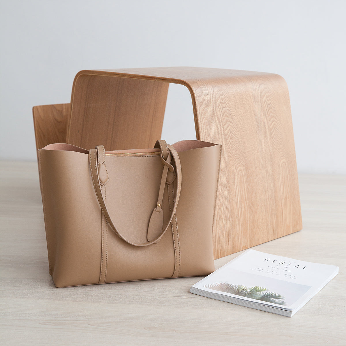 Beige leather tote bag with wooden stool on a light wooden surface