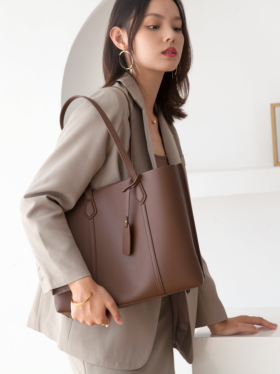 Woman holding a brown leather handbag against a plain background