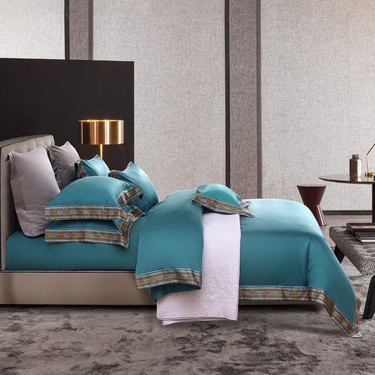 Teal bedspread with patterned trim on a bed in a stylish bedroom.
