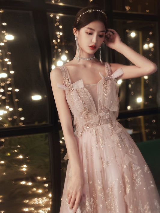 Woman in a pink evening gown with floral details against a softly lit background