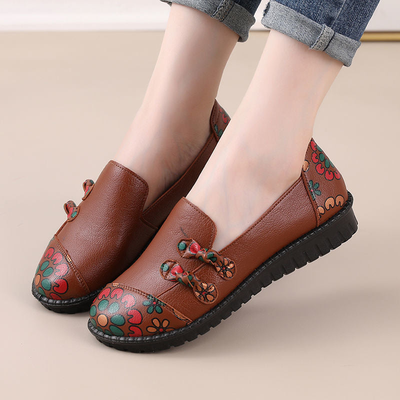 Brown loafers with floral patterns worn by a person on a beige background