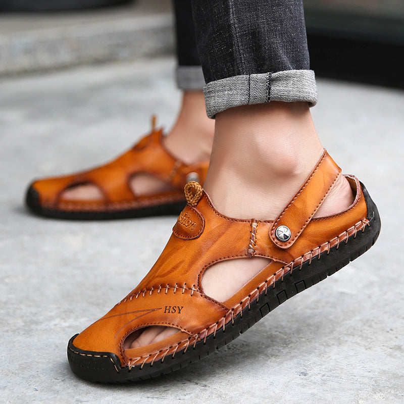 Brown leather sandals worn with rolled-up jeans on a concrete surface