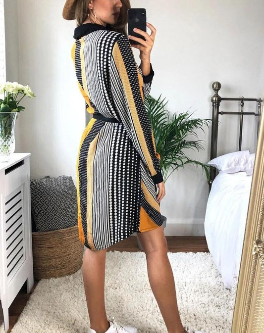 Woman taking a mirror selfie wearing a patterned dress in a bedroom.