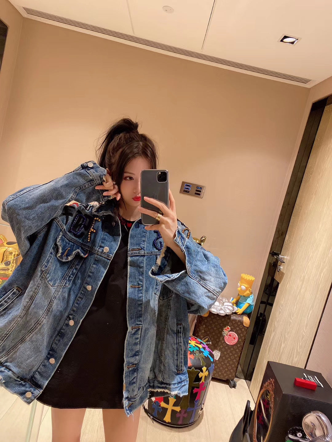 Person wearing a denim jacket taking a mirror selfie in an indoor setting.