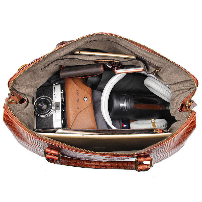 Open leather bag with camera, phone, and other items on a white background