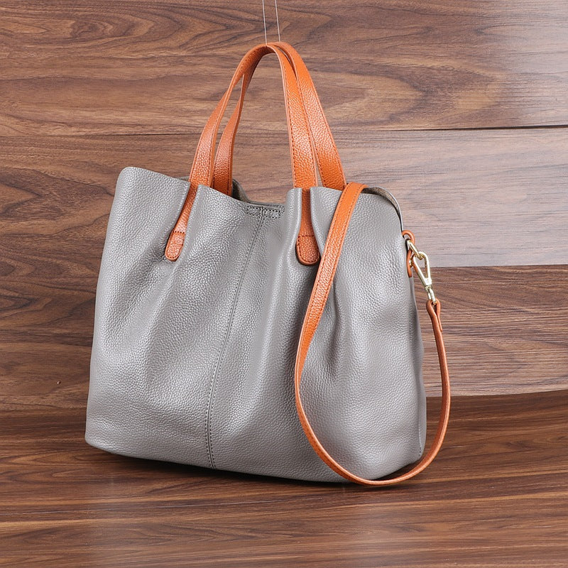 Gray handbag with orange handles and strap on a wooden surface