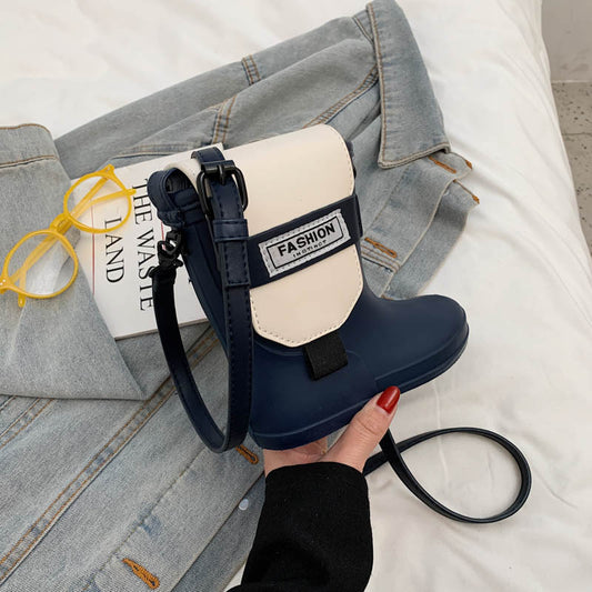 Navy and beige handbag with 'Fashion' label held by a hand on a light gray surface with denim jacket and glasses.