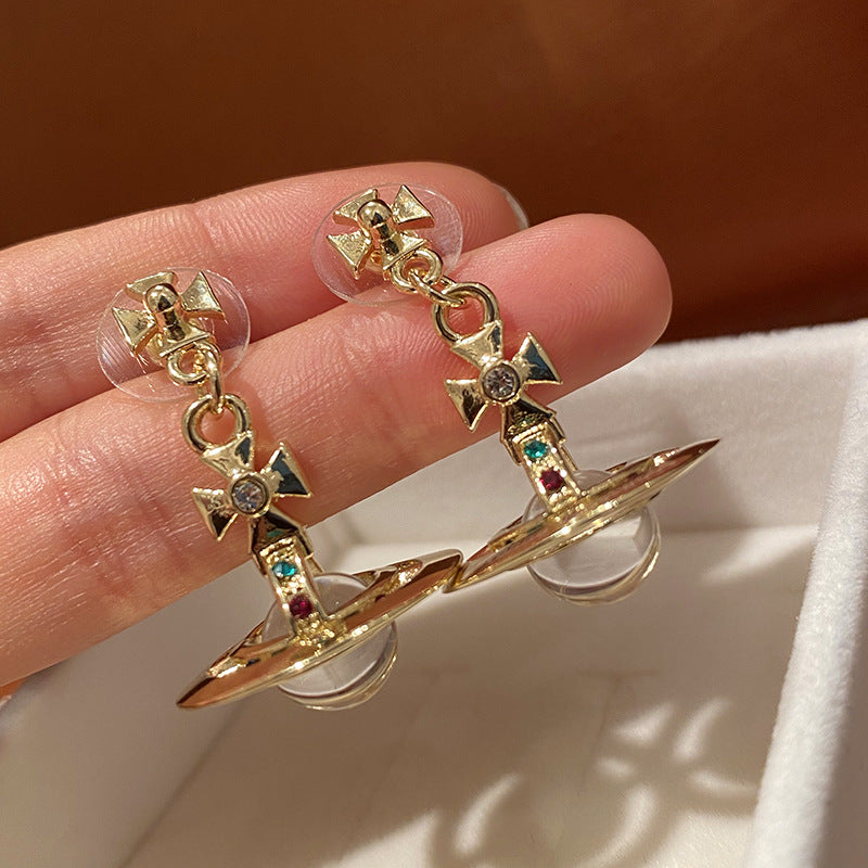 Gold earrings with gemstones held between fingers against a neutral background