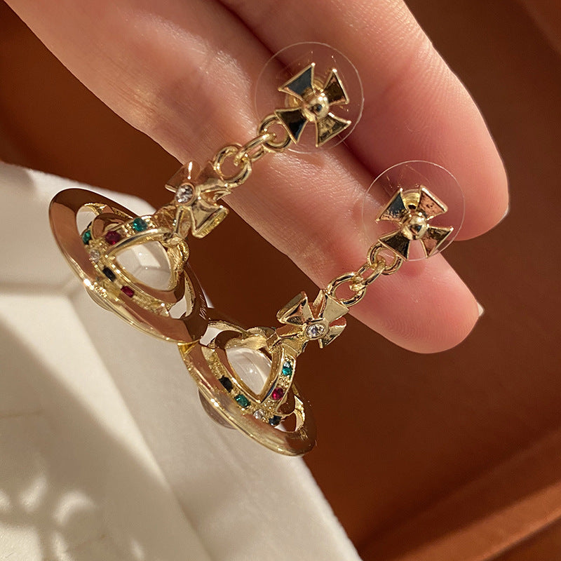 Gold earrings with gemstones held between fingers against a neutral background