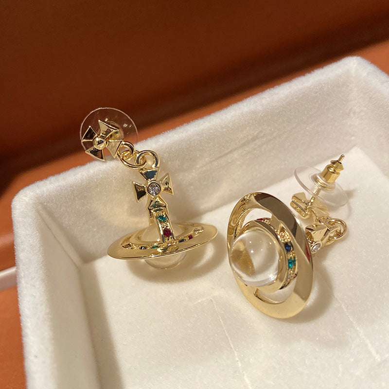 Gold earrings with colorful gemstones on a white cushion
