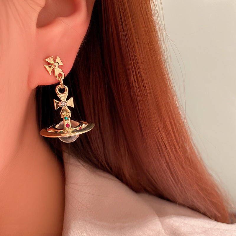 Gold earring with gemstones worn by a person with long hair.
