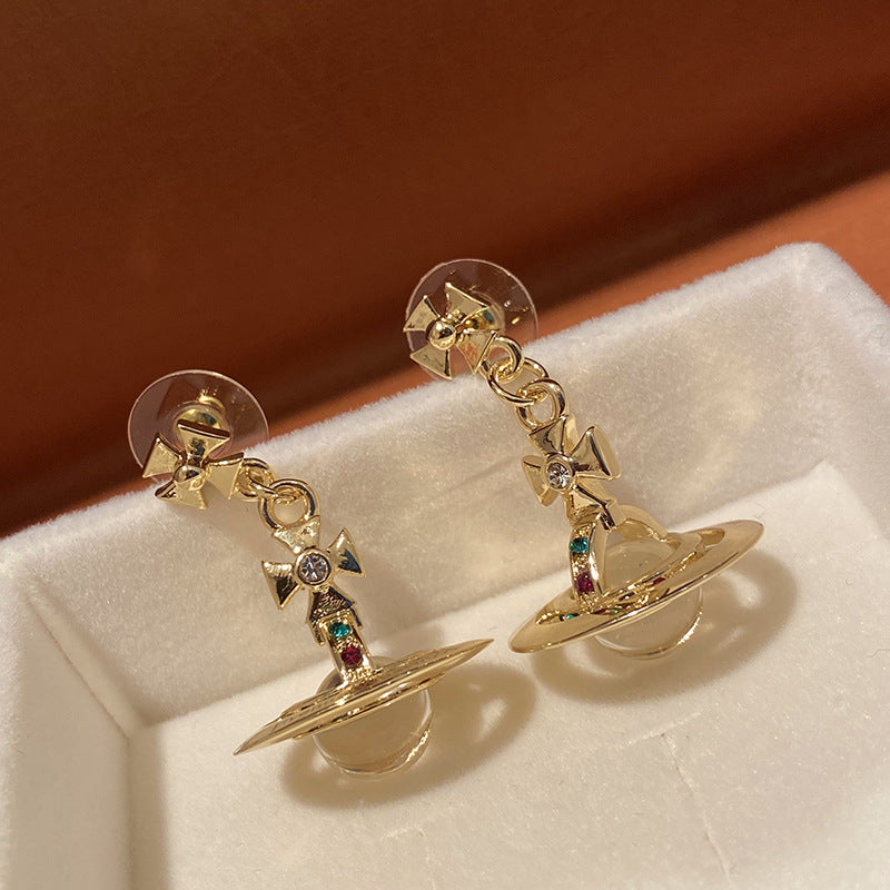 Gold earrings with gemstones on a white cushion