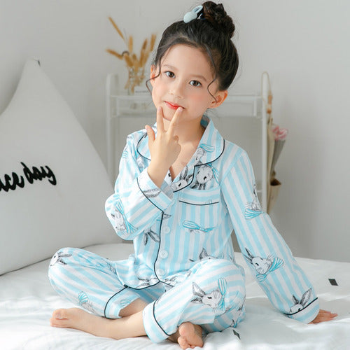Child wearing a light blue pajama set with animal prints on a white bed.