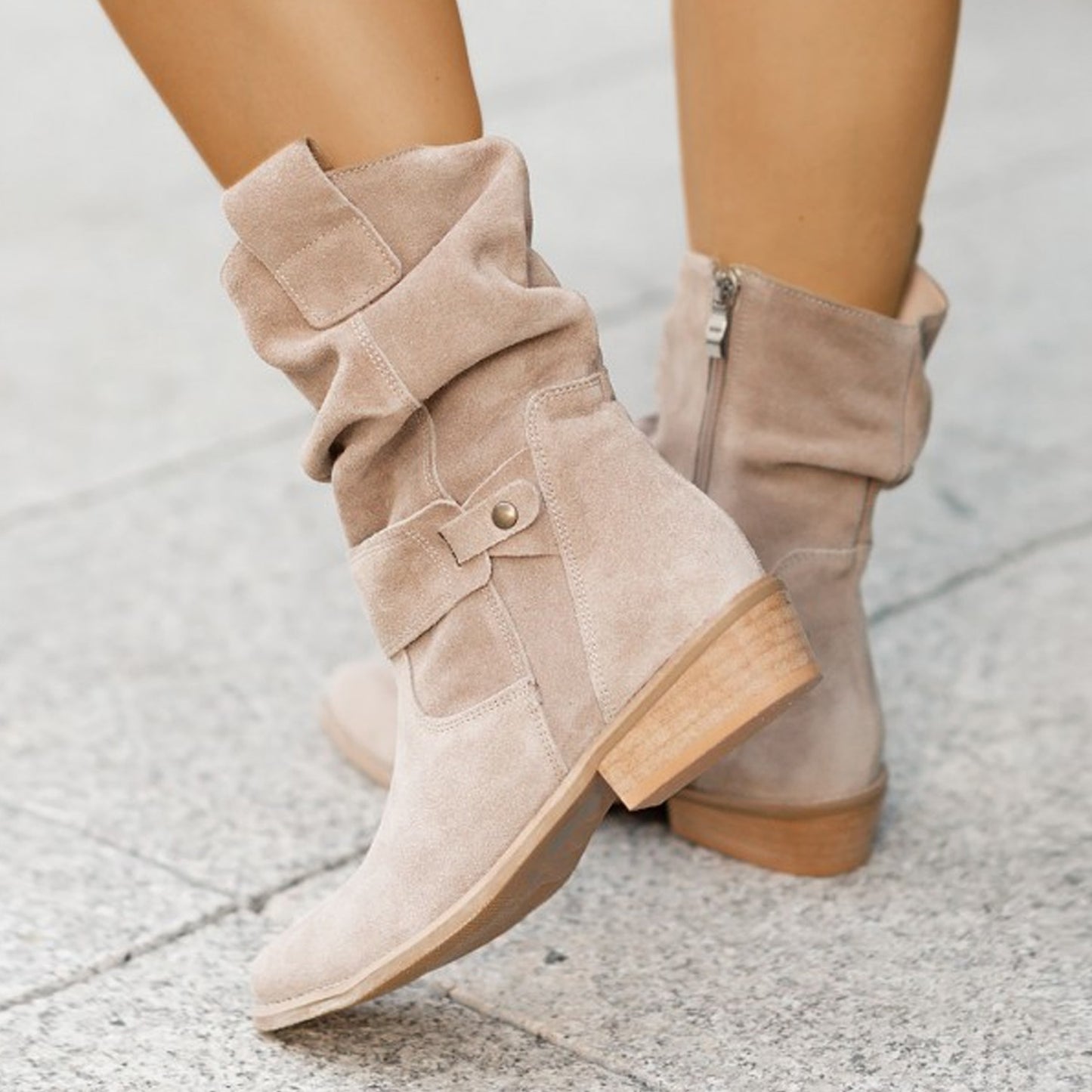 Beige suede boots with a button detail on a light gray pavement background