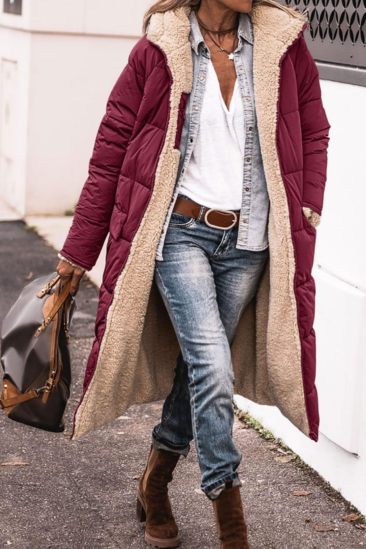 Person wearing a long burgundy puffer coat with beige lining, blue jeans, and brown boots.