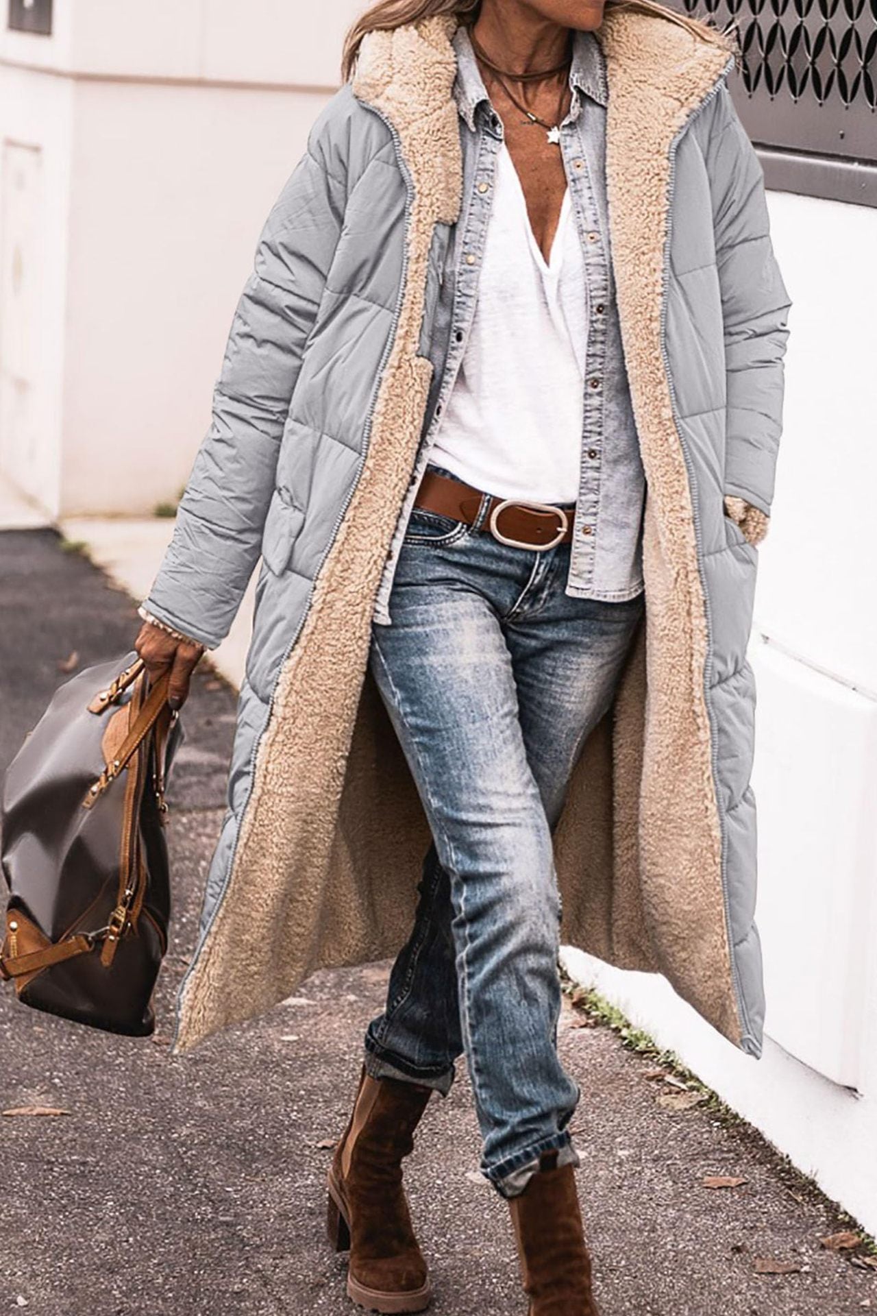 Person wearing a long gray puffer coat with beige lining, white shirt, blue jeans, and brown boots.