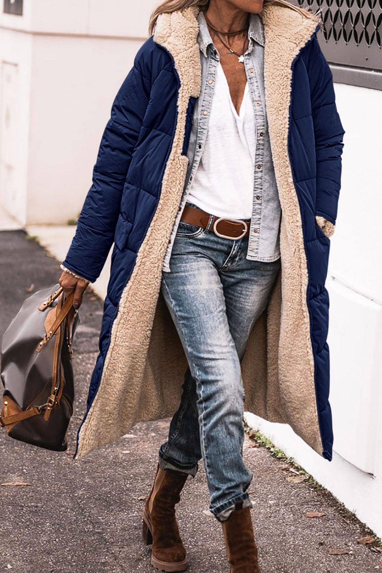 Person wearing a long navy coat with beige lining, white shirt, blue jeans, and brown boots.