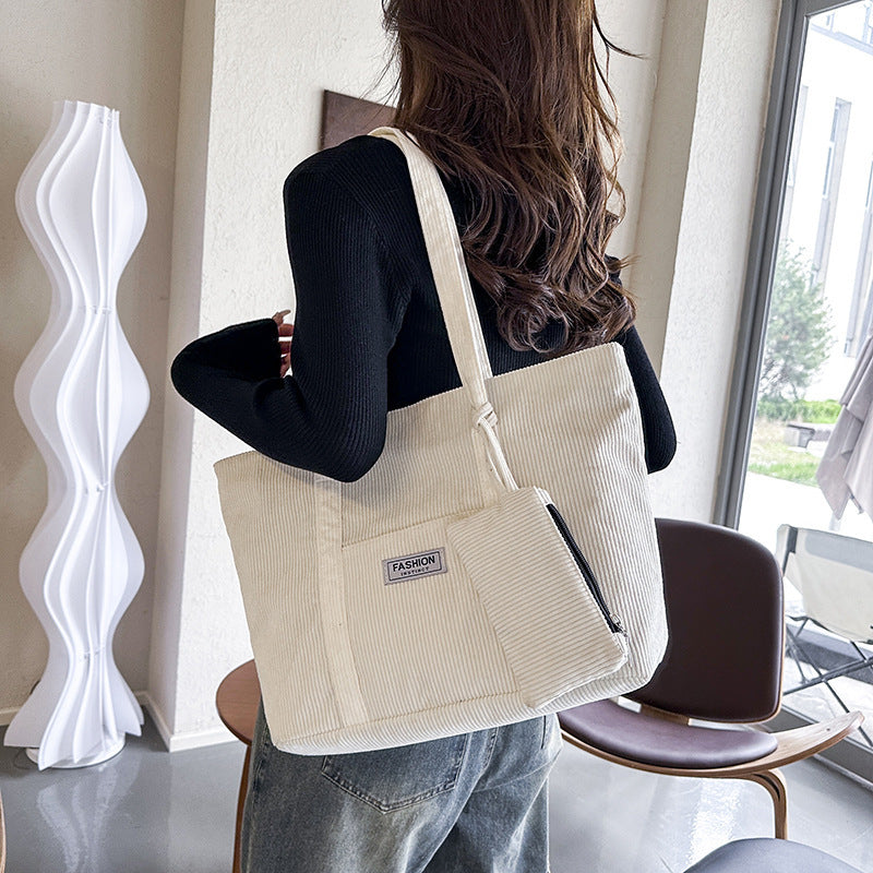 Person holding a beige tote bag with a visible brand label in an indoor setting.