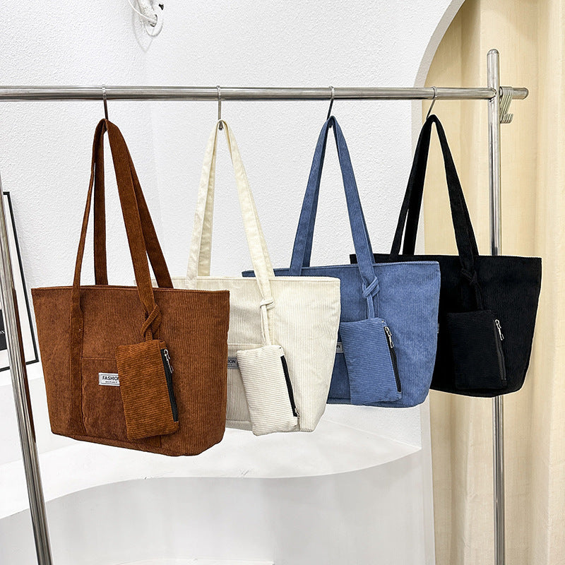Four bags in brown, white, blue, and black hanging on a rack against a white background.