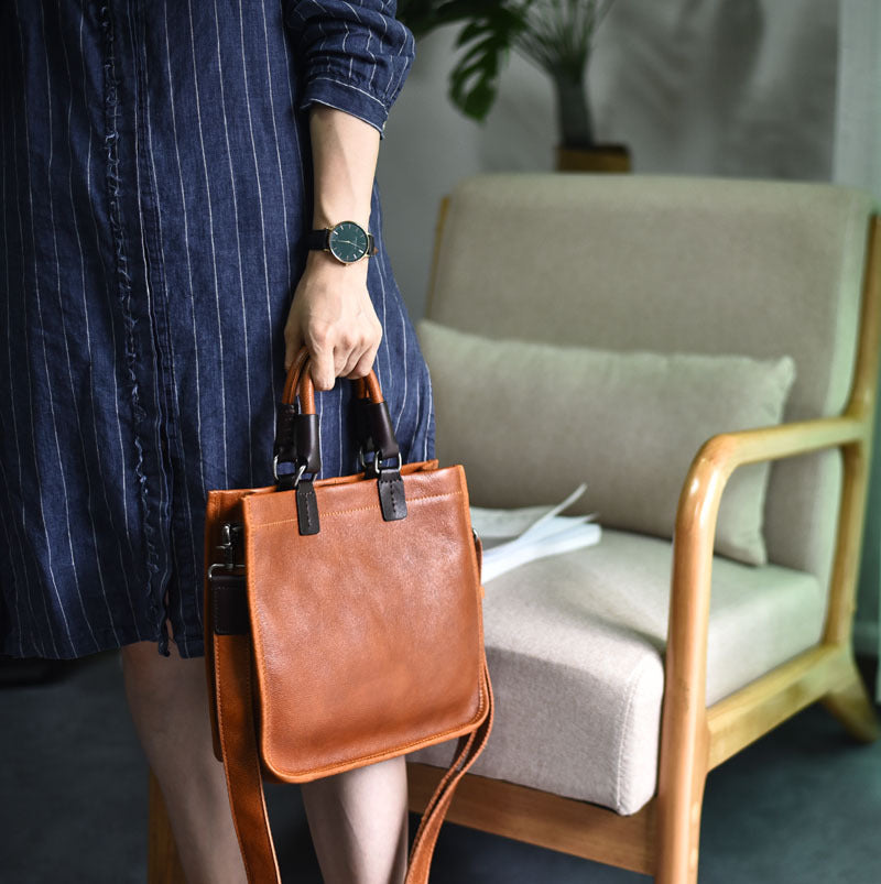 Person holding a brown leather bag in a room with a chair and plant.