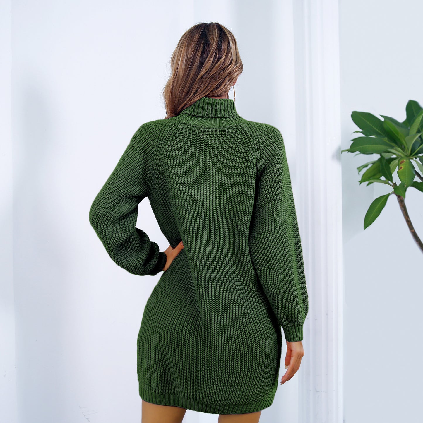 Green knitted dress worn by a person against a white wall with a plant on the right. by millivan