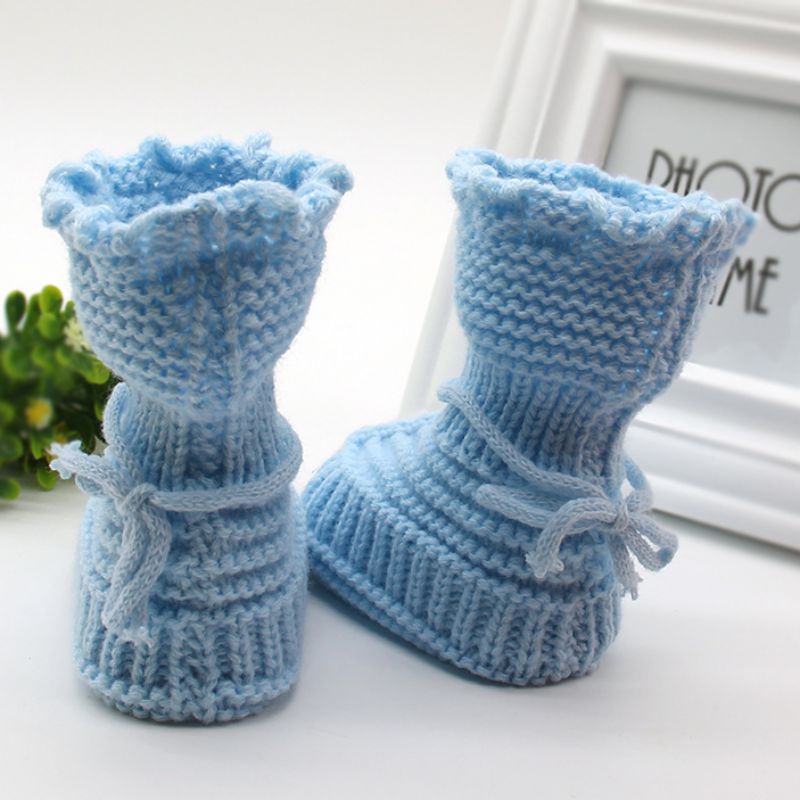 Pair of blue knitted baby booties on a white surface with a blurred background.