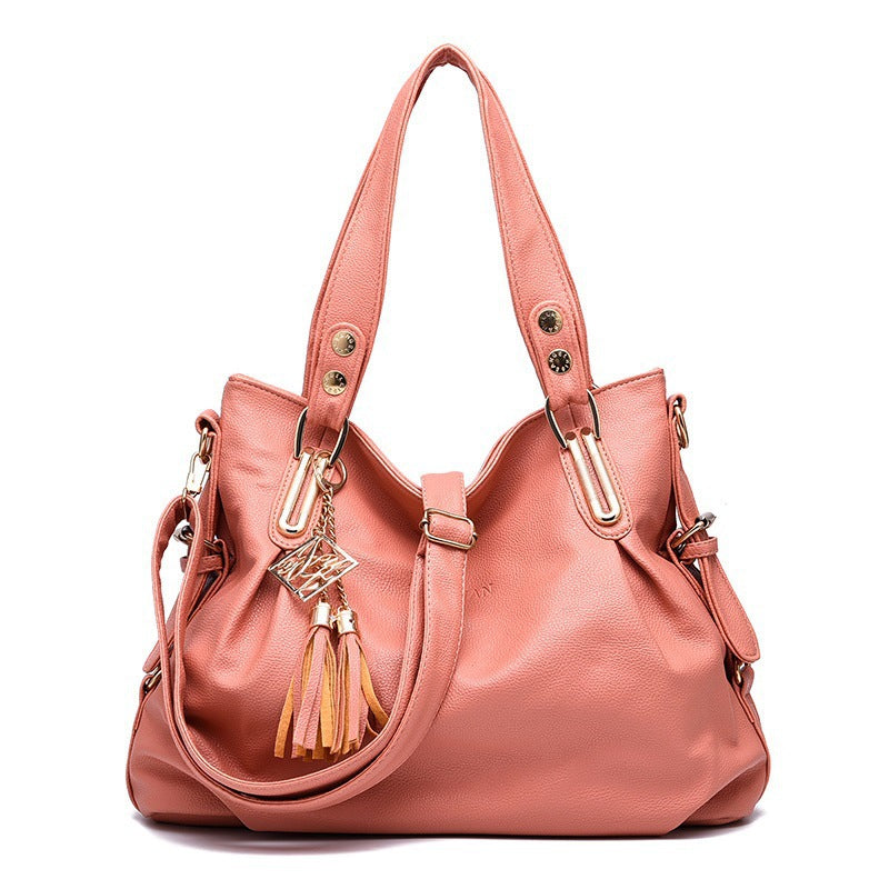 Pink handbag with gold accents and tassels on a white background