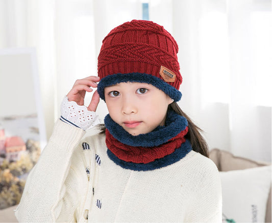 Child wearing a red and blue knitted hat and scarf set indoors.