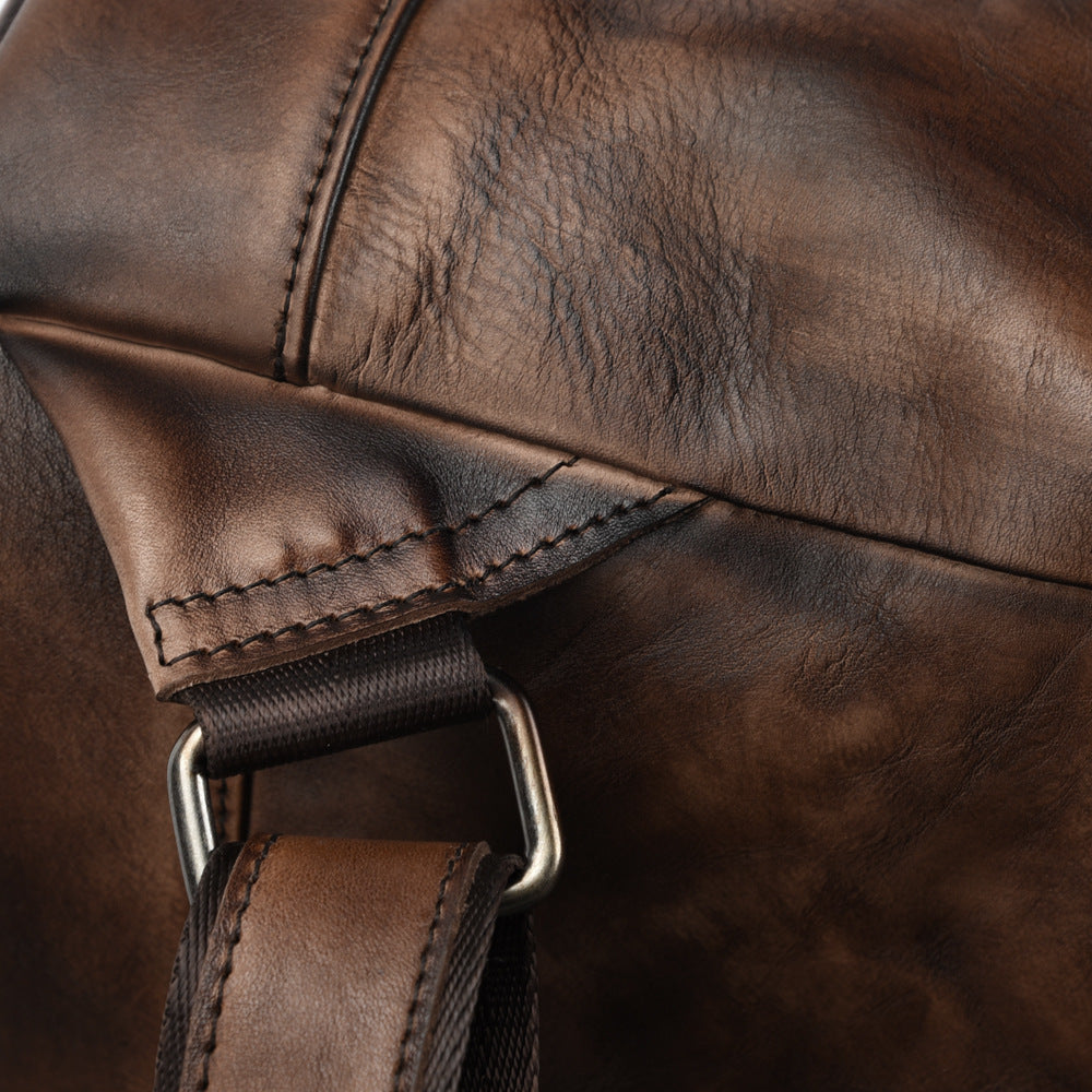 Close-up of a brown leather bag with a strap and buckle.