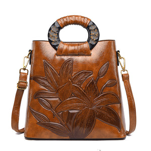 Brown leather handbag with floral embossing and decorative handle on a white background