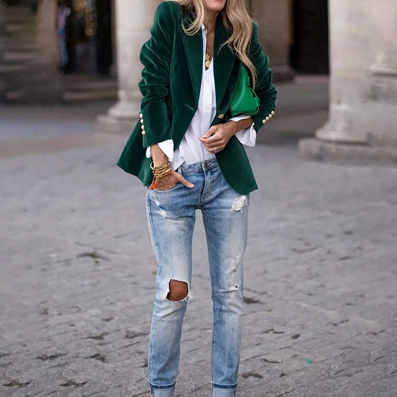 Person wearing a green blazer, white shirt, and ripped jeans on a street.