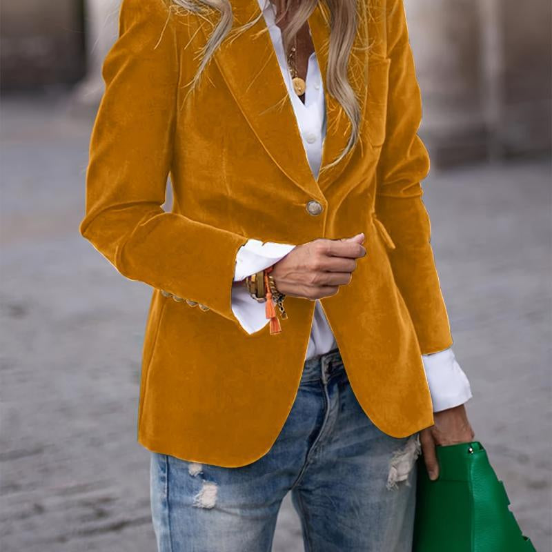 Person wearing a mustard yellow blazer over a white shirt with blue jeans and a green handbag.