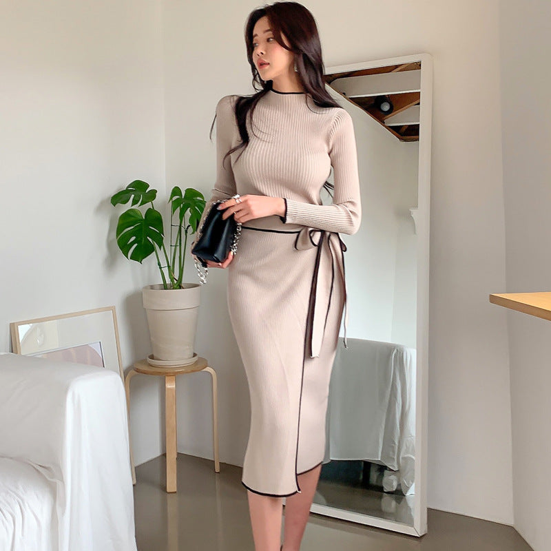 Woman in a beige dress standing in a room with a mirror and plant.