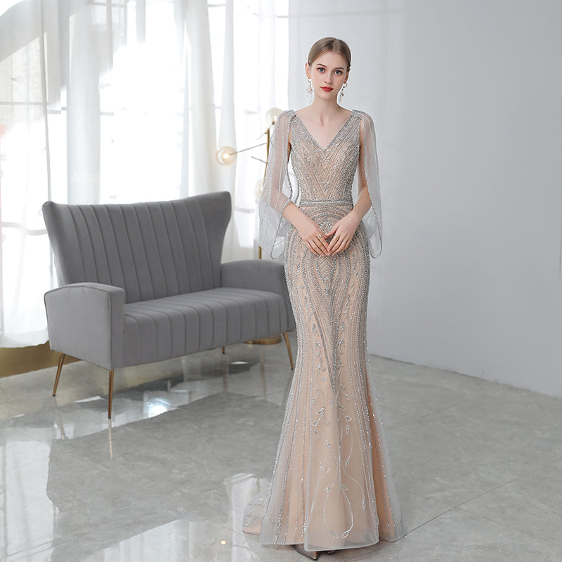 Woman in a beaded evening gown standing in a modern room with a gray sofa.