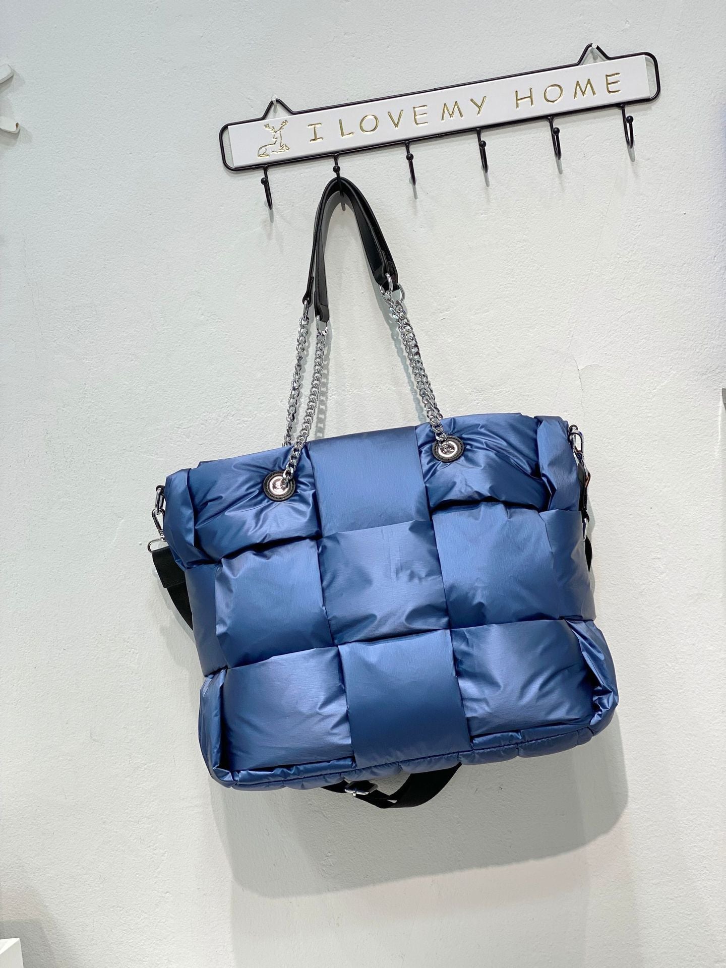 Blue quilted handbag with chain detail hanging on a wall hook.