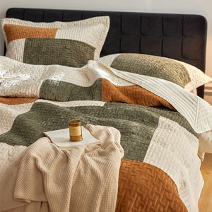 Bed with a quilted comforter and pillows in neutral colors, featuring a candle on a nightstand.