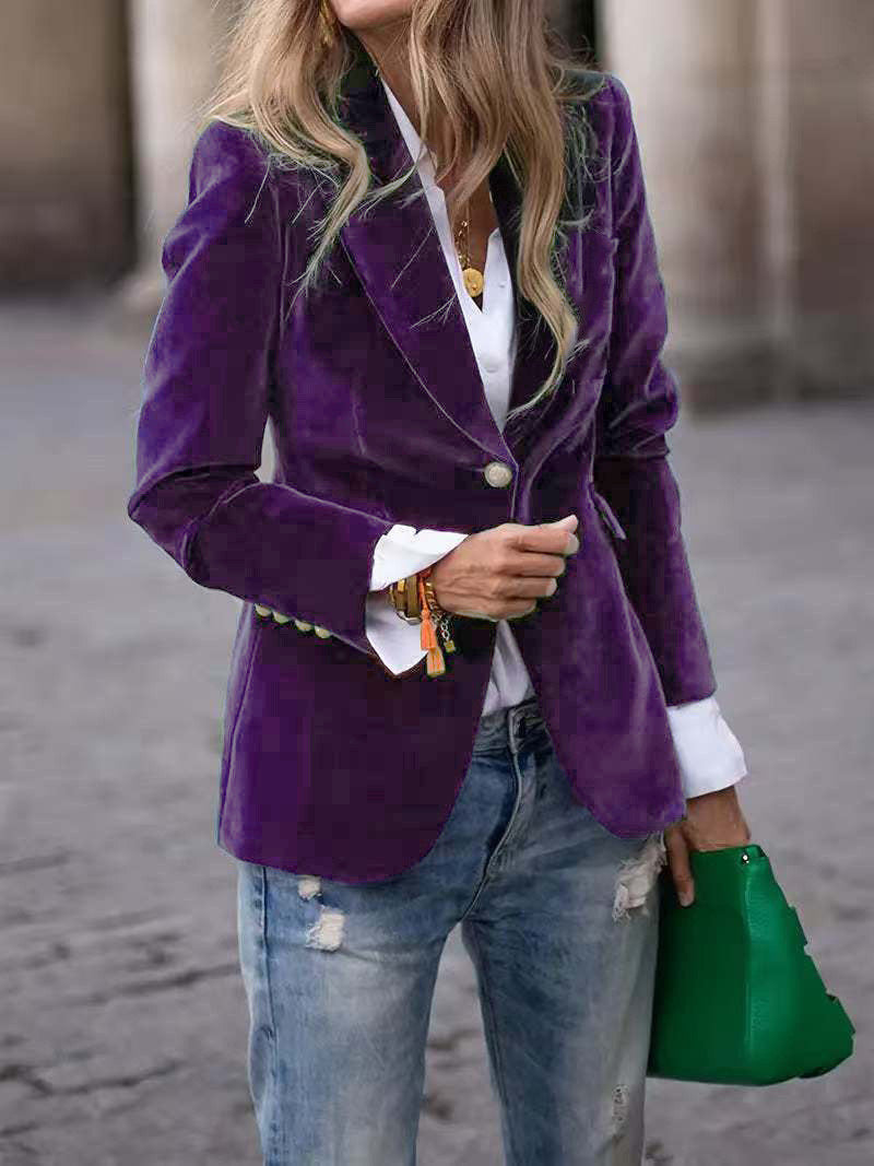Person wearing a purple velvet blazer with a white shirt and blue jeans, holding a green handbag.