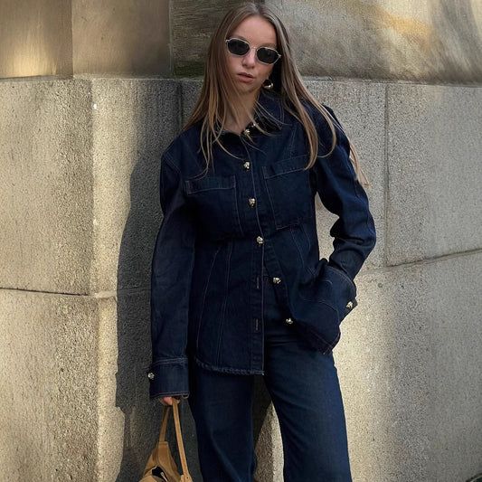 Person wearing a dark denim jacket and pants against a stone wall.