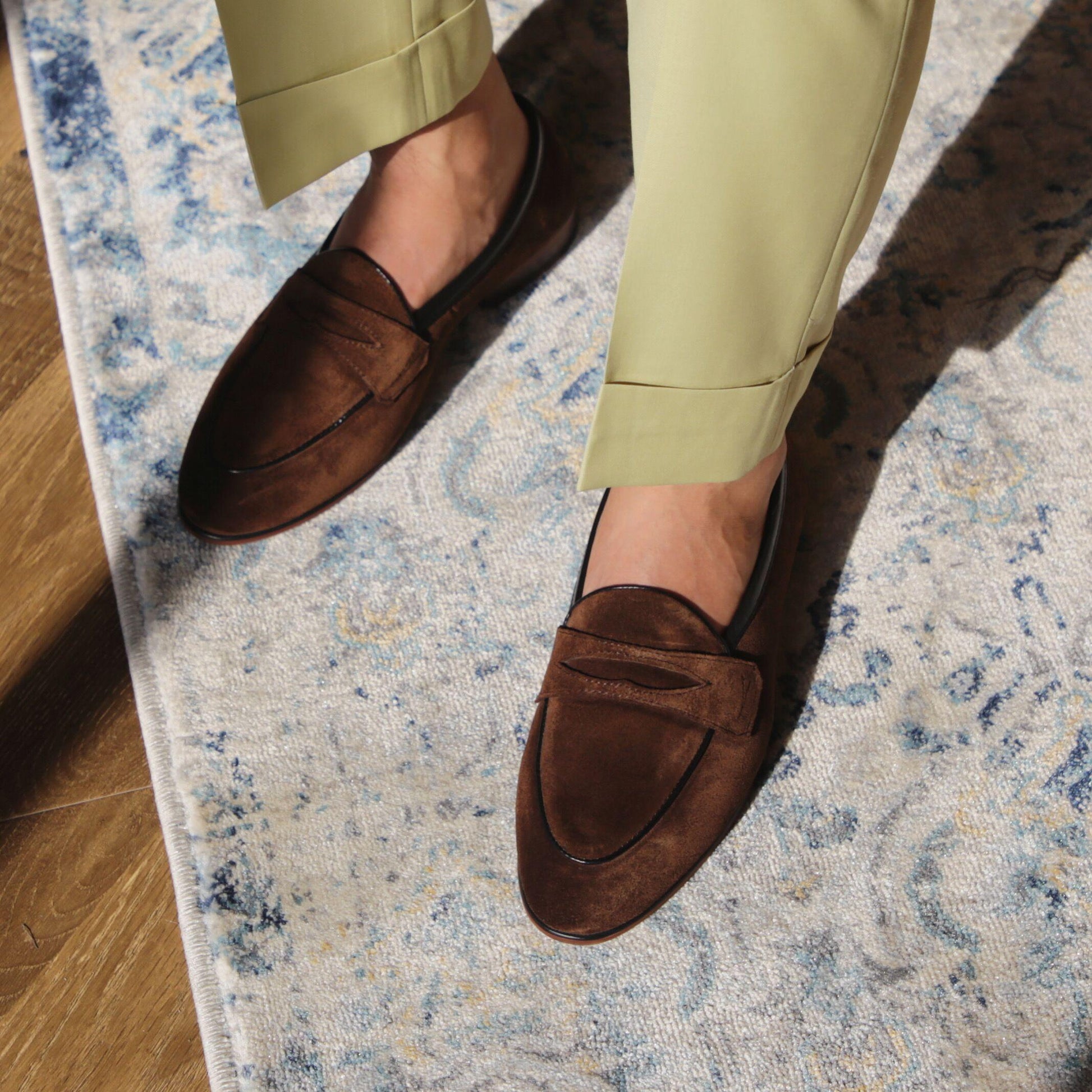 Brown loafers worn with light green pants on a patterned rug.