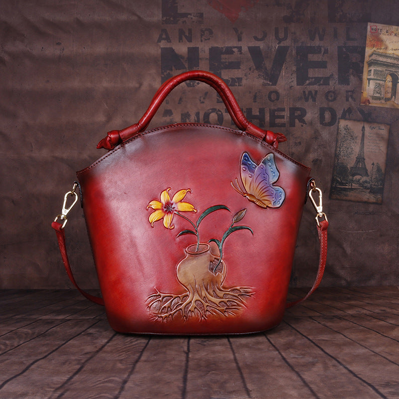 Red leather handbag with floral and butterfly design on a wooden floor.