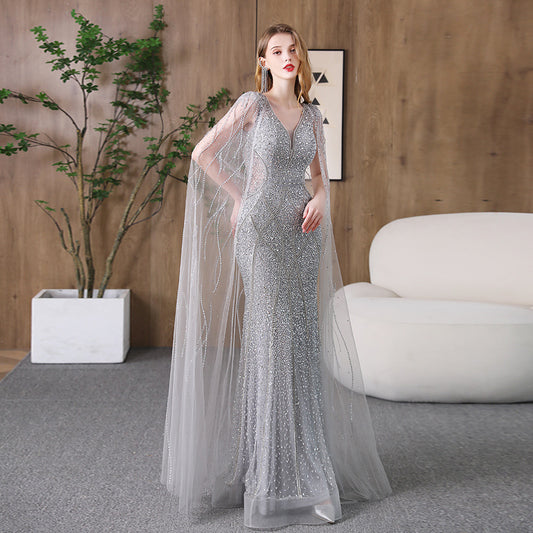 Woman in a silver evening gown standing in a modern room with a plant and sofa.